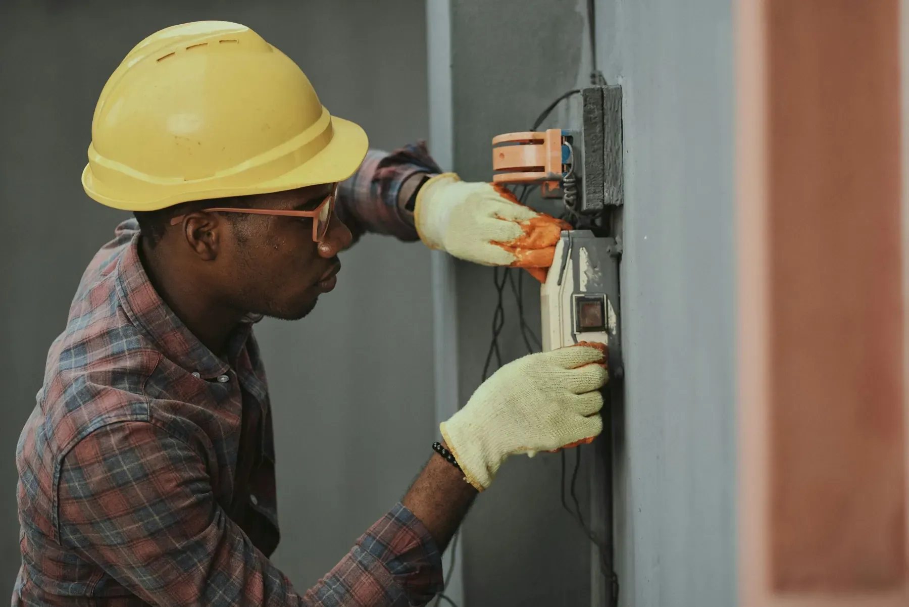 An electrician in a hard hat installing a wall receptacle during a rewiring job